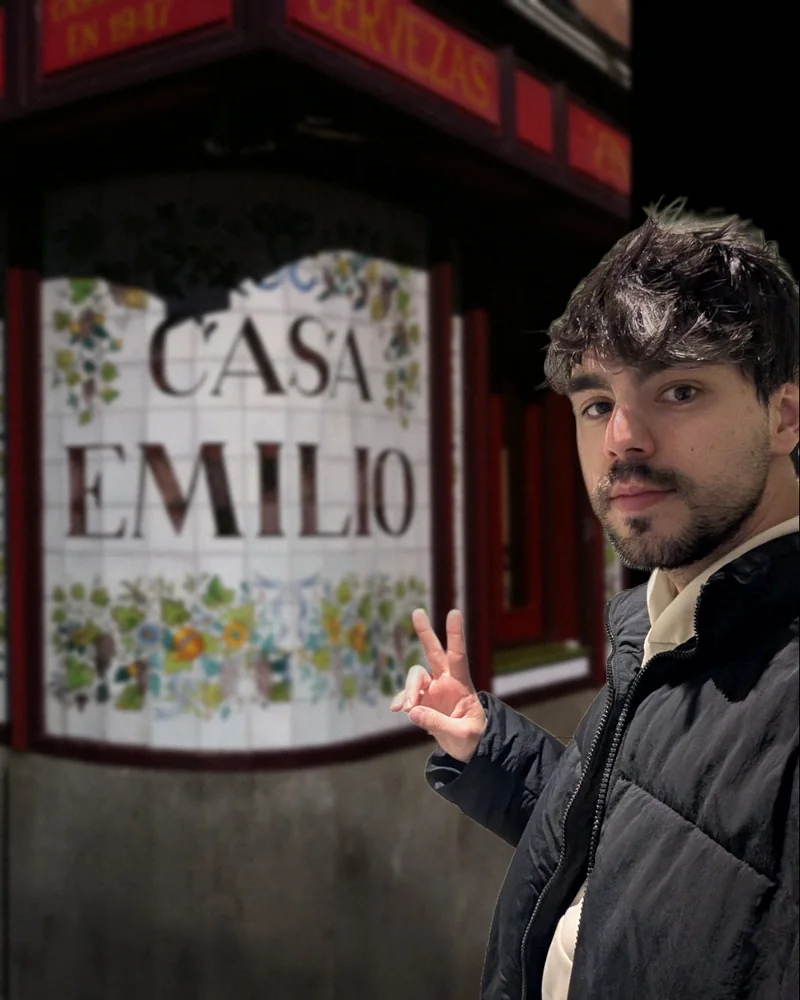 Alejandro haciéndose un selfie y saludando con dos dedos delante del rótulo de azulejos de Casa Emilio